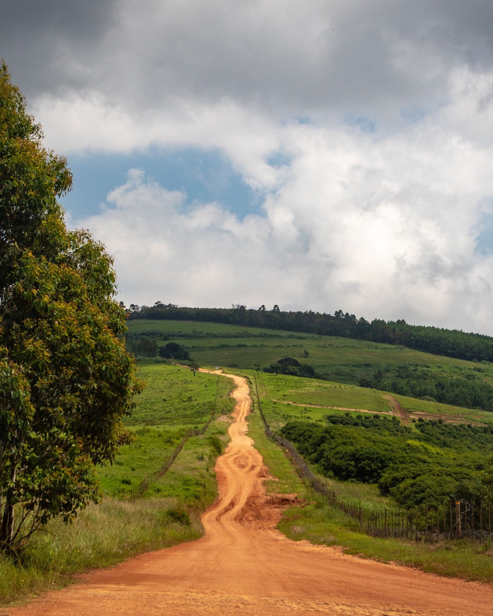 A murram road climbing into green hills under a storm sky